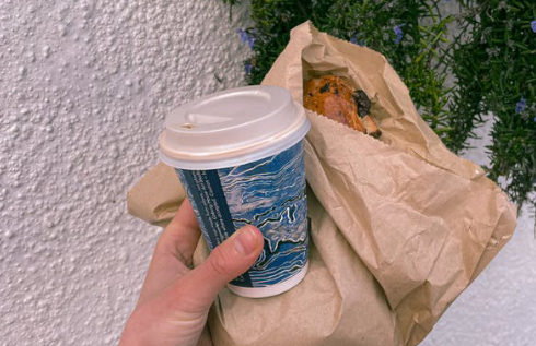 Person with takeaway coffee and bakery in paper bag